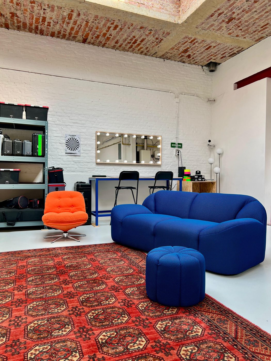 De leefruimte met blauwe zetel, oranje fauteuil en de make-uphoek met spiegel